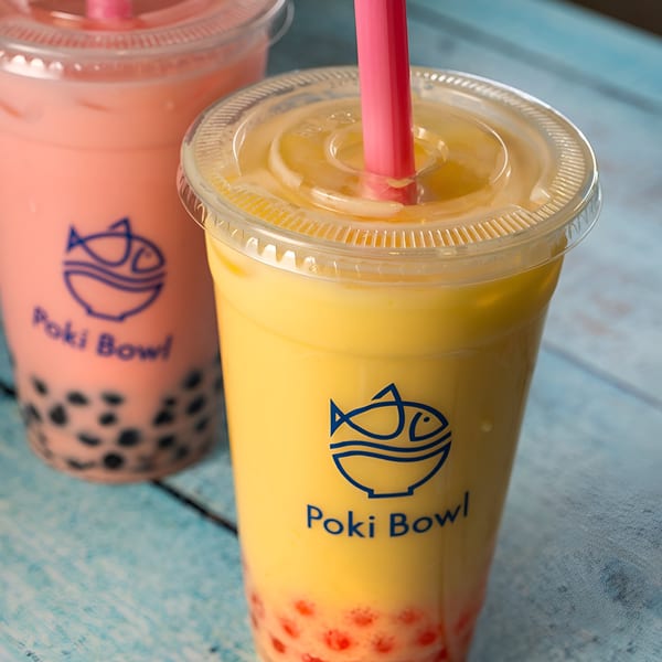 Two Poki Bowl bubble teas, one yellow with red boba, one pink with black boba.